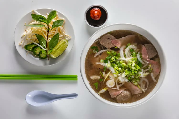 Overhead view of beef pho with a side plate of bean sprouts, basil, jalapeños and lime